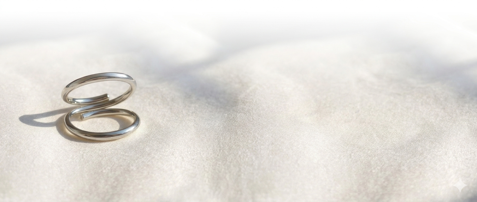 Two Splendint sterling silver rings on white sand, wide horizontal banner shot